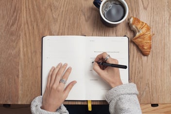 a pair of hands writing in a journal 