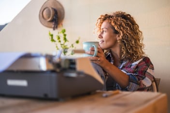 woman sitting with mug and typewriter looking out