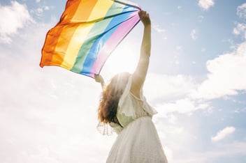 a woman holding up the rainbow pride flag toward sunlight