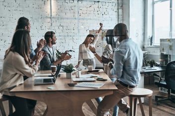 woman raising her fist while team members clap hands in a meeting room 