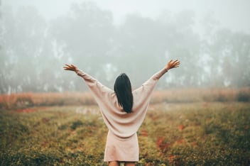 woman raising hands in front of grassy field and fog