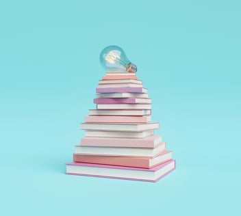 pyramid of books with lightbulb on top against a sky blue background 