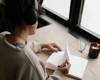 a woman writing in a journal at a desk with headphones