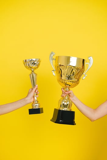 Two women holding two trophies that celebrate their achievements.