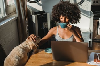 A woman sips her coffee and pets her dog while working.