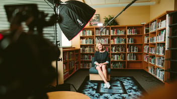 Woman sitting in front of book shelve ready to be interviewed under lighting