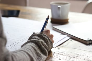 person writing on paper at desk 