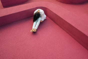 woman sitting leaning forehead into knees on pink floor