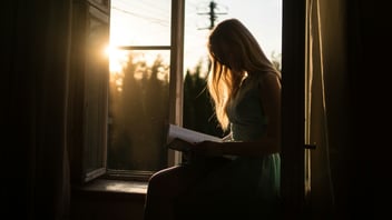 woman sitting next to window reading 